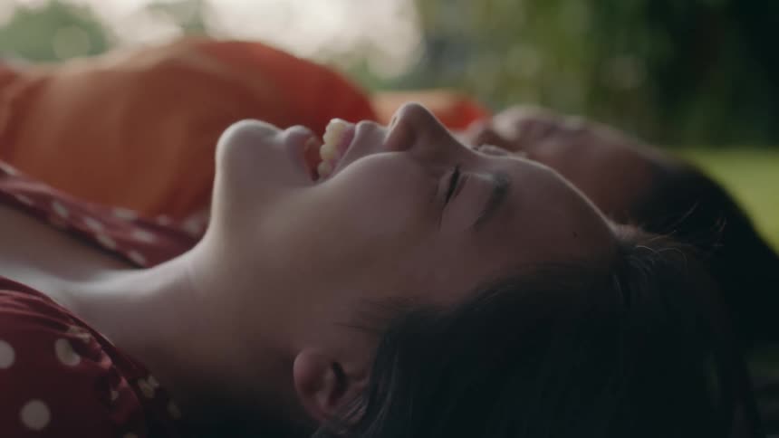 An up close of two womens faces laying on their backs outdoors laughing and smiling