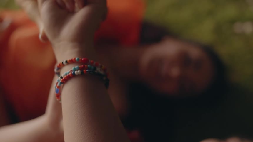 Two friends laying on the green grass admiring colorful bracelets on their wrists