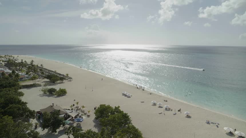People enjoy a sunny and beautiful topical beach as a jetski carves through turquoise water