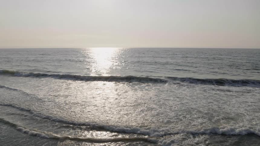 Slow push over gentle breaking waves rolling onto shore from sparkling open ocean that stretches to the horizon