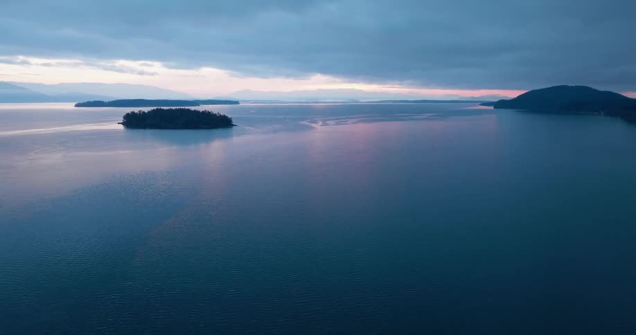 The first light of dawn paints the sky and calm ocean water dotted with small islands