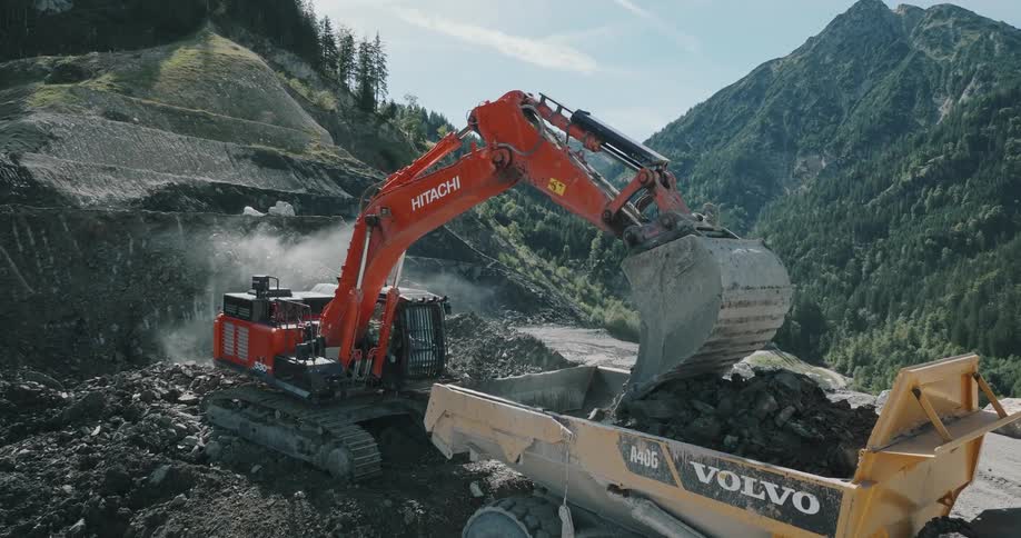A bulldozer dumps rocks into a trash receptacle on a mountain