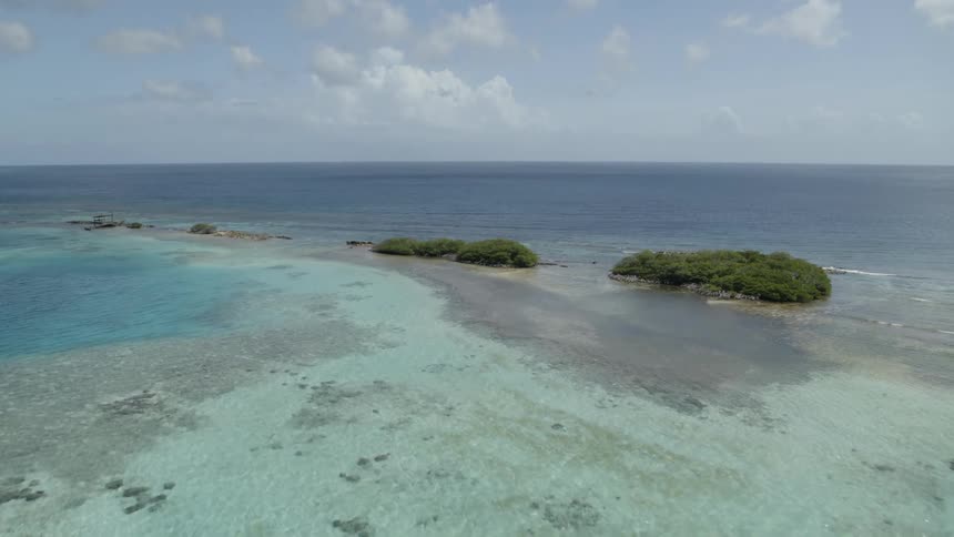 Ascending from just above the surface of tropical blue water over small mangrove islands and shallow reefs