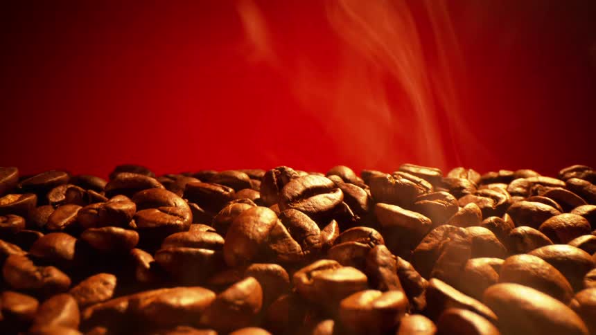 Coffee beans laid out with steam rolling off them with a red background