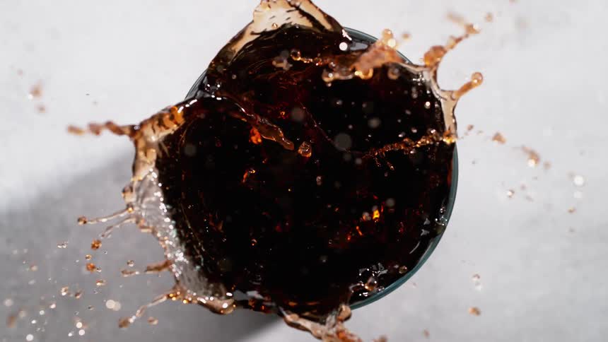 Three ice cubes fall in slow motion and splash into a drink