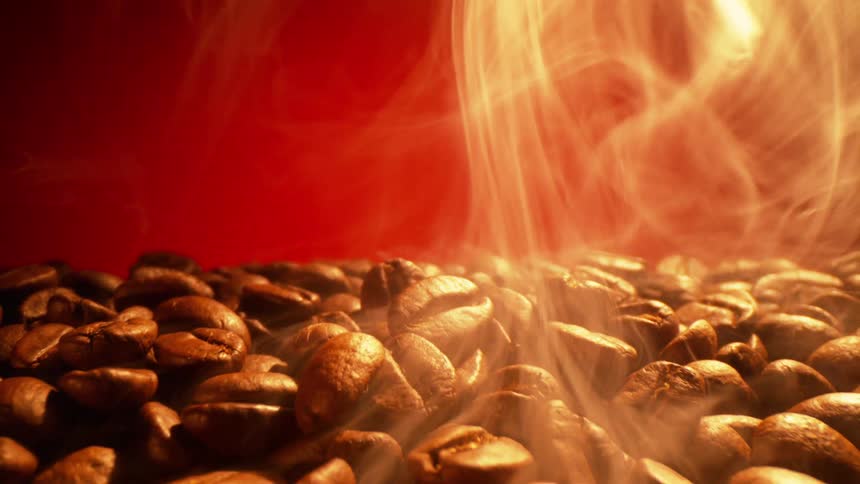 A clsoe up of coffee beans with steam rolling off them against a red backdrop