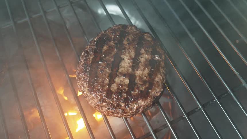 A black grill opens to reveal three juicy burgers cooking over a charcoal fire