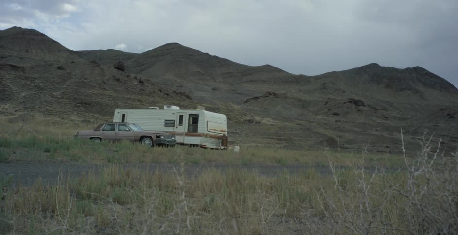A camper and a car parked next to each other in the middle of nowhere in front of a mountain range