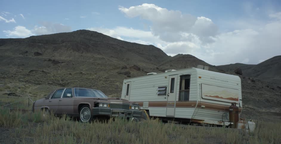 A car and trailer are parked by the mountain