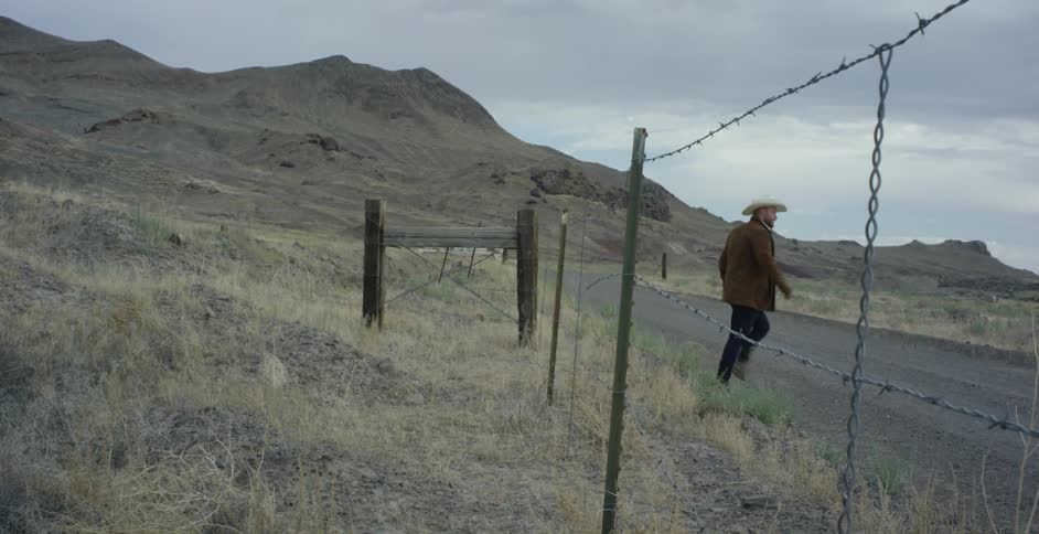 A sense of isolation and solitude permeates the scene as a lone man can be seen crossing a fence and walking down a lonely road