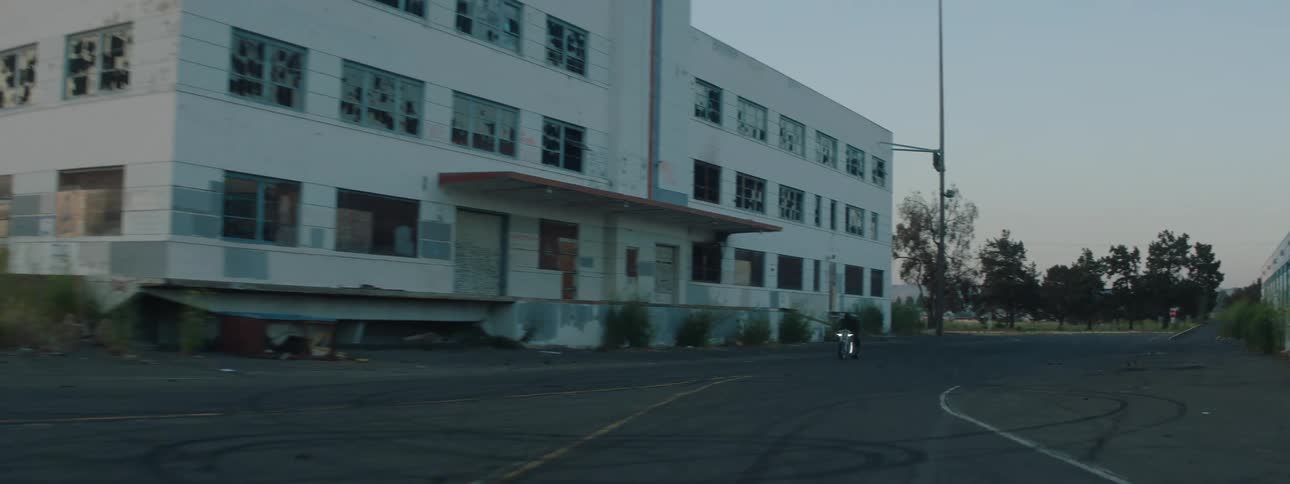 A person rides a motorcycle around abandoned buildings at morning