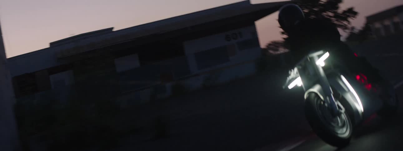 A persons silhouette driving a motorcycle at dusk through buildings