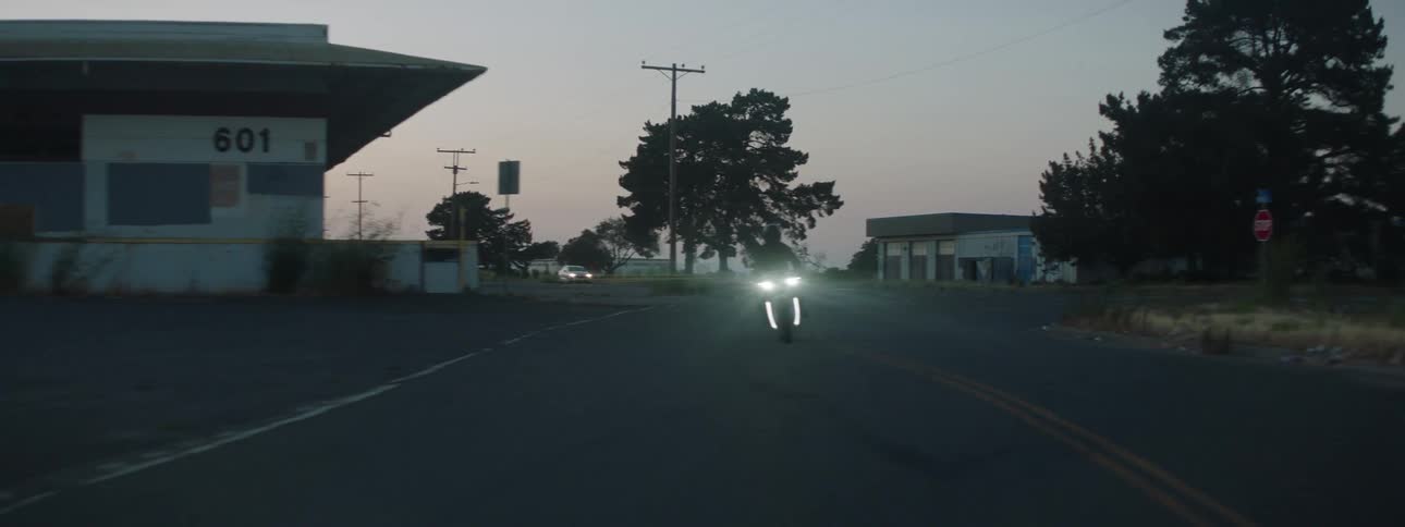 Person on motorcycle traveling along the highway through a rural town at sundown