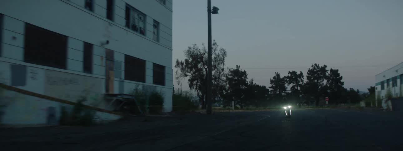 A person riding a motorcycle through an area with abandoned buildings at dusk