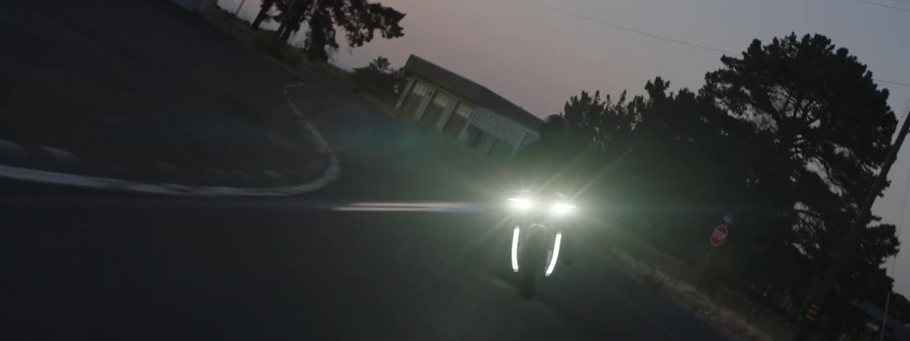 A person is riding quiclky around a curved road in a suburban neighborhood on a motorized bike as it begins to get dark