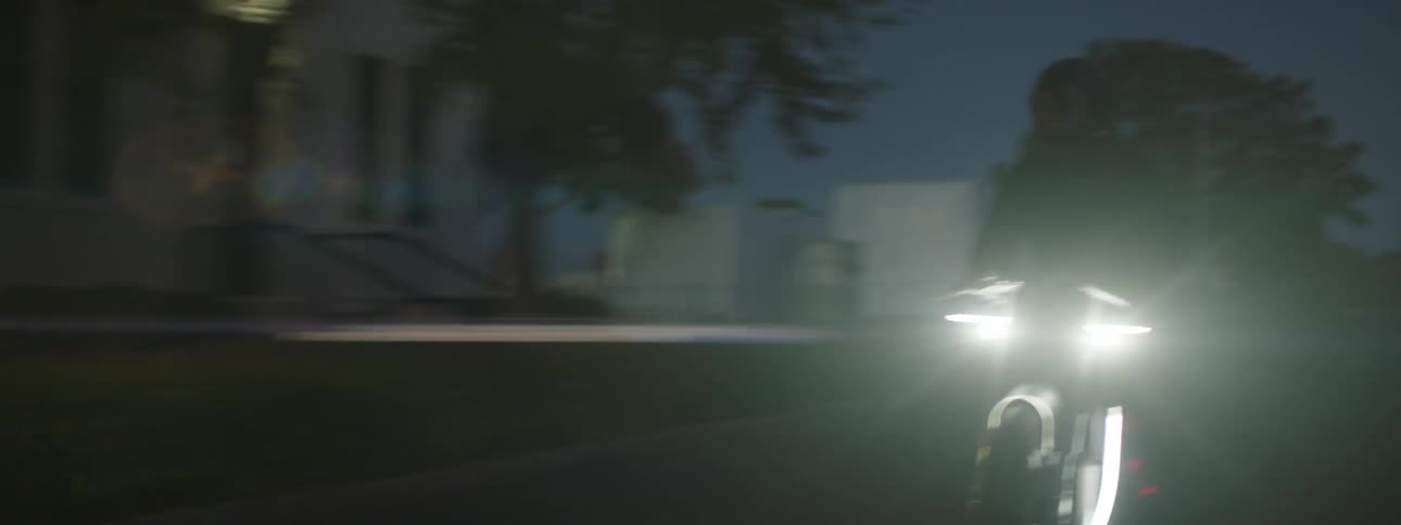 A person rides a motorcycle with headlights on at night on the city streets