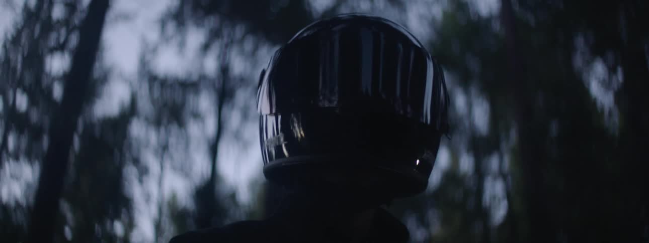 A person wearing a black full face helmet with trees behind them