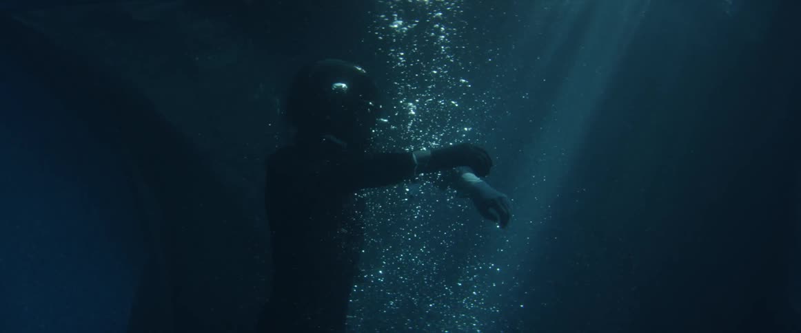 Person wearing crash helmet rises through bubbles toward surface at night