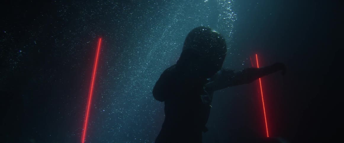 A person in a black suit and helmet underwater floating around red lasers