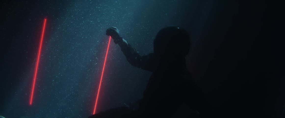 A man wearing all black floating in water in front of red lasers