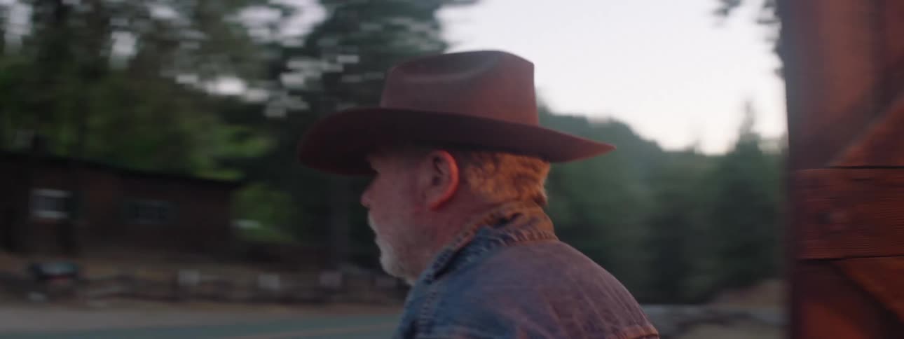 Man wearing cowboy hat walking out of barn to house across the road