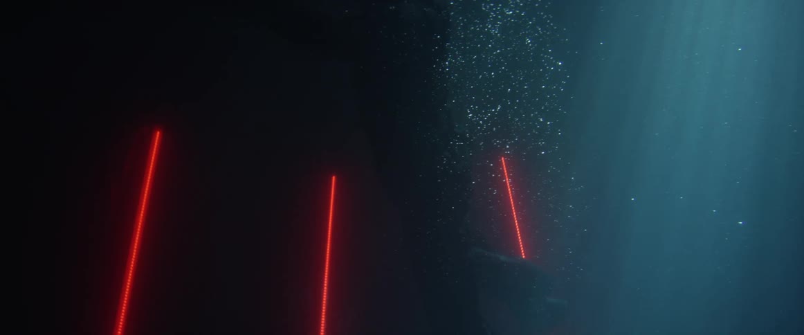 Person wearing a crash helmet floats in dark water near three strips of red light