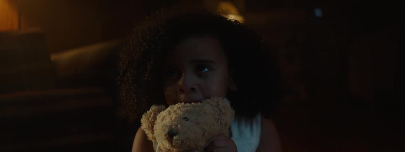 Girl huddles with teddy bear staring in dimly lit room