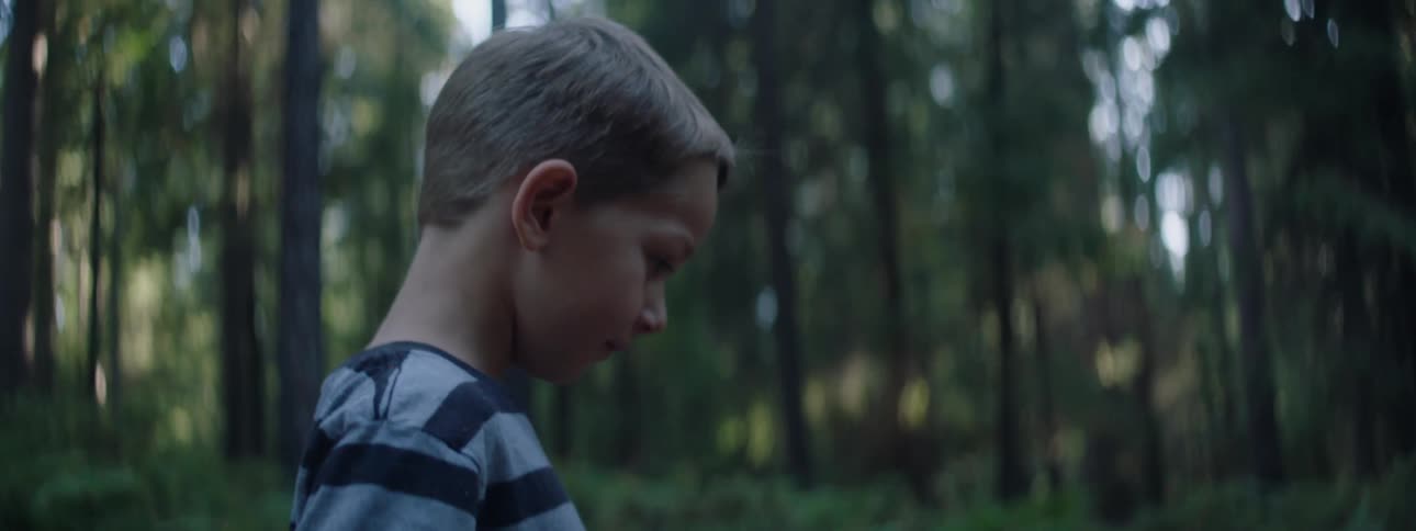 A sad young boy walks alone through a forest in the day