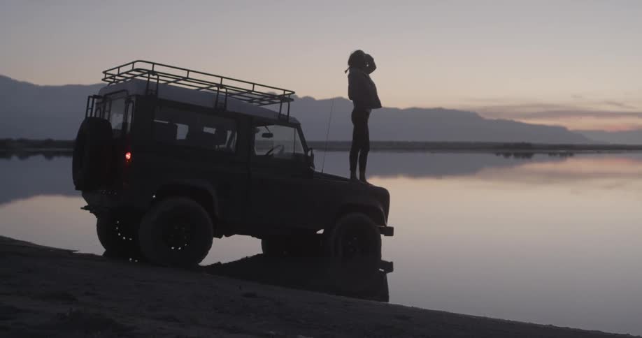 A woman stands on a truck by the water