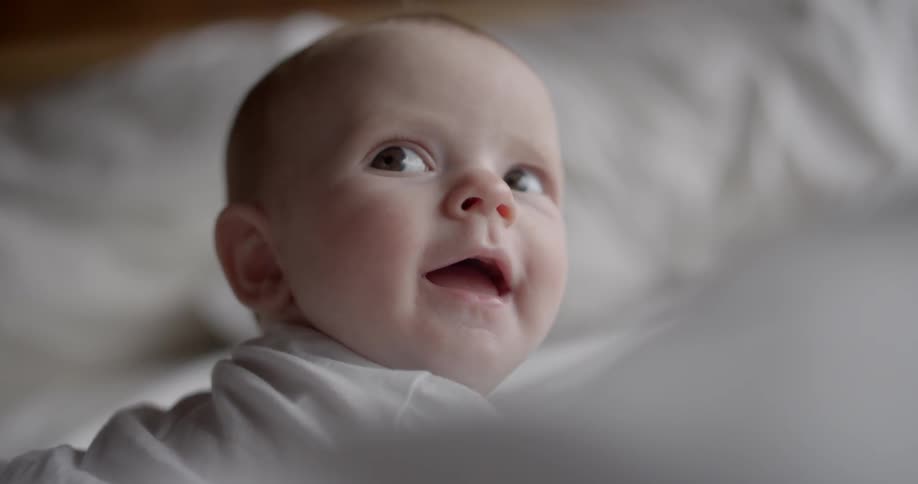 A baby looks up from the bed