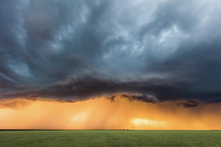Dark storm clouds hang low and move in rotation over rural land in a deep yellow sky as lightning flashes
