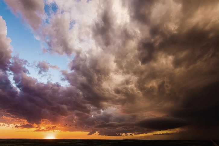 Dark storm clouds move across an orange sky as the sun shines brightly on the horizon