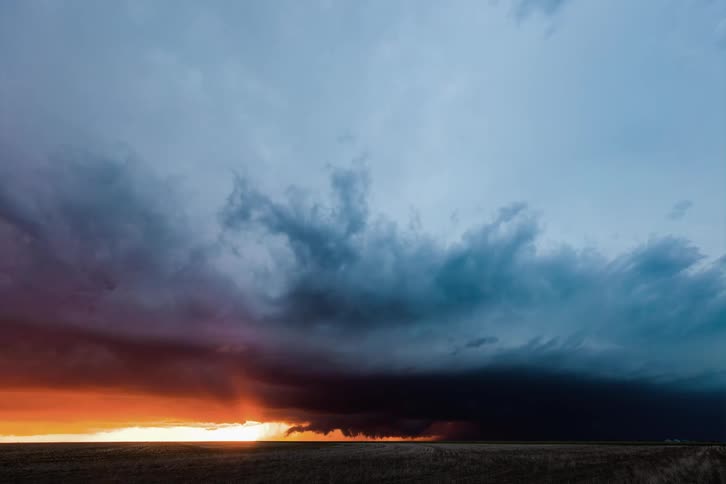 A huge blue mass of clouds come together forming a vortex swirling around with lightning within it