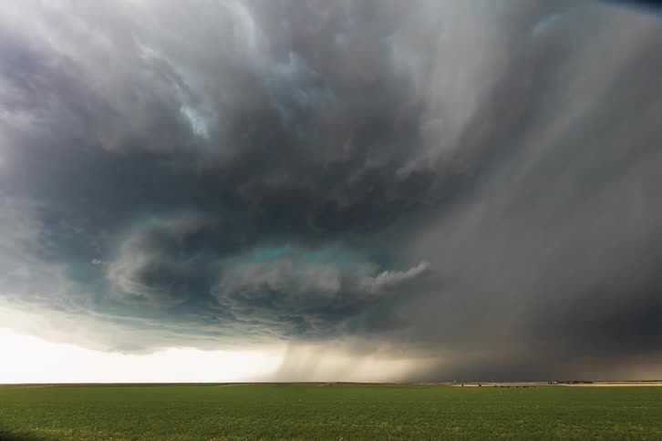 Dark storm clouds move in rotation over a field as lightning flashes
