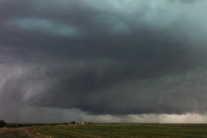 Dark storm clouds are moving in rotation and pouring rain as traffic moves on a rural road