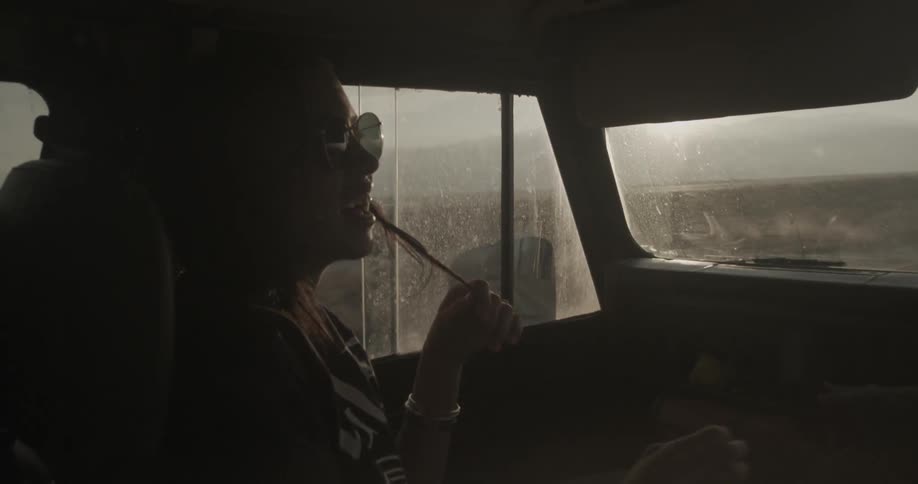 A woman is sitting in the back seat of a moving vehicle pointing and laughing