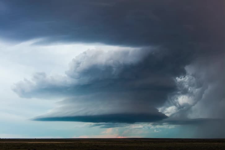 Dark storm clouds are moving in rotation over rural land as lightning flashes and strikes the ground