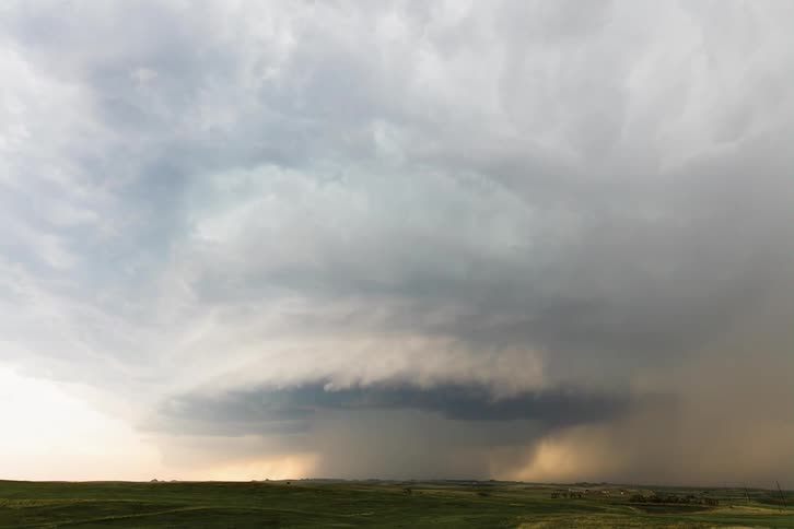 Dark storm clouds move in rotation over a field as rain pours down from the clouds