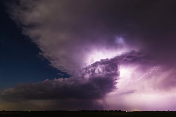 Lightning flashes wildly inside of dark storm clouds glowing purple as they move across the sky