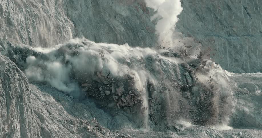 The side of a mountain being blasted with dynamite in slow motion