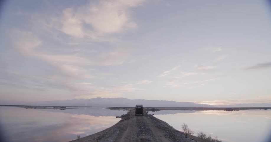 A truck drives on a strip of land between two bodies of water