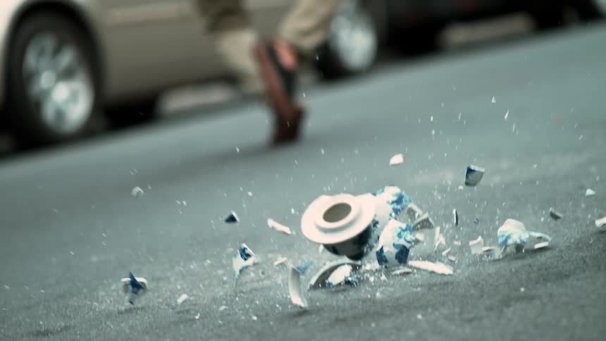 A man contorts, avoiding a vase that falls to the ground and smashes