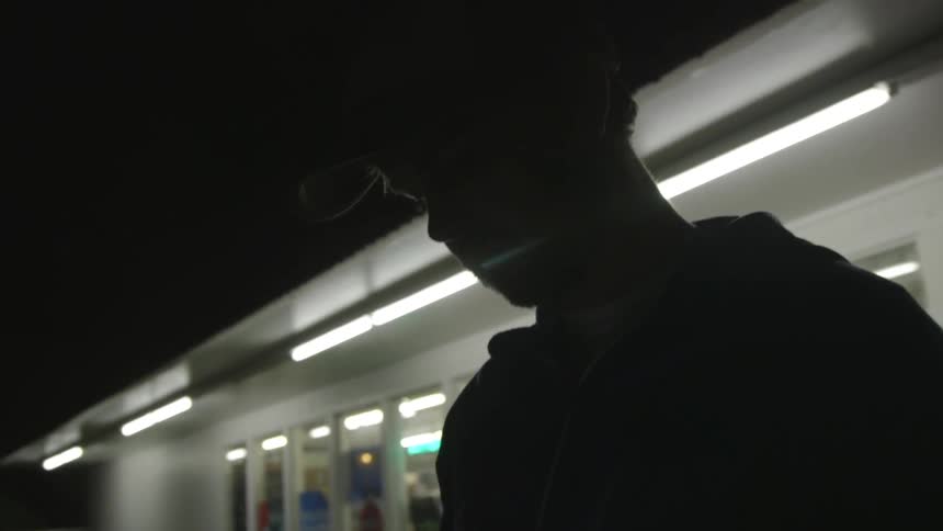 A man uses is phone in front of a store at night