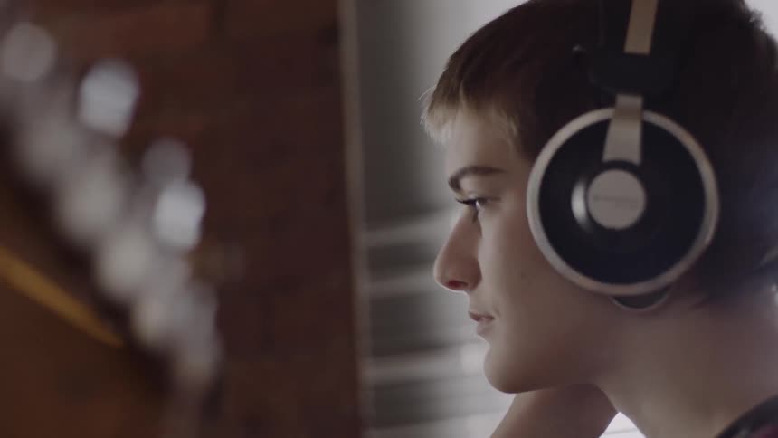 A woman wearing headphones holds a guitar and bobs her head