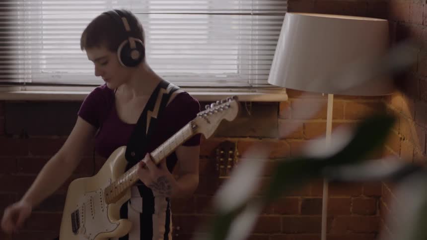 Woman wearing headphones plays the guitar and types on laptop
