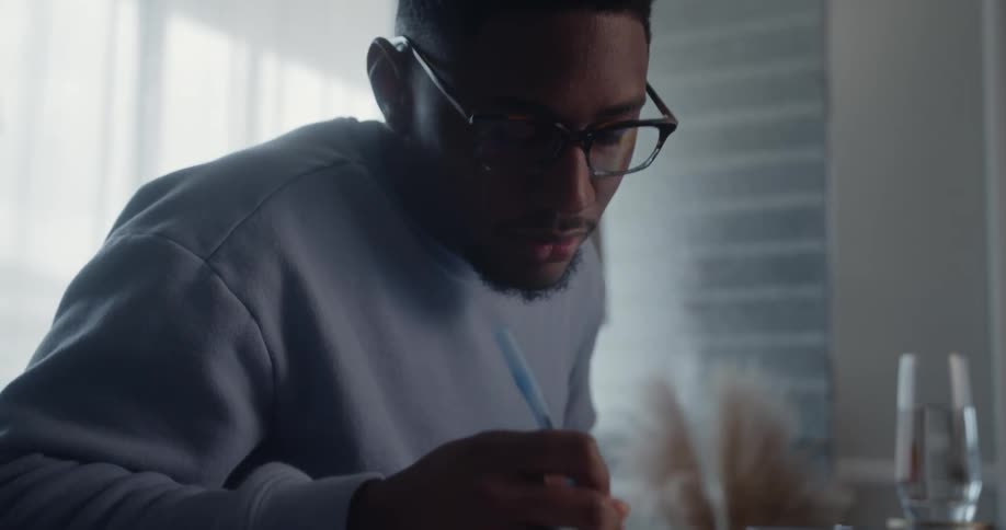 A young man concentrates before he begins to write using a pen