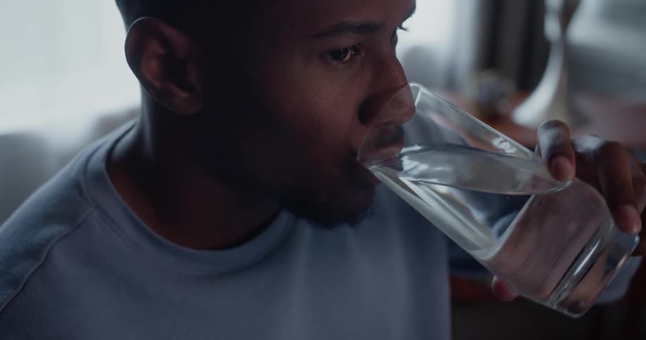 Man with blue sweater drinks a glass of water