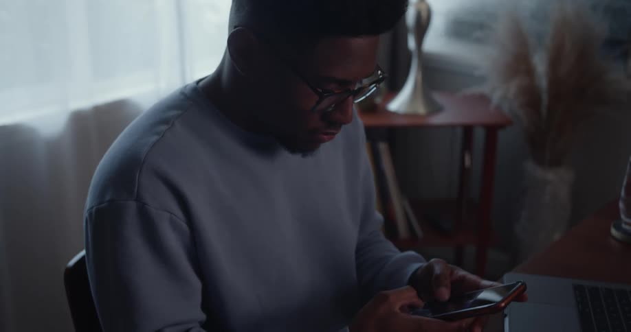 A man texts on his phone while sitting at his desk
