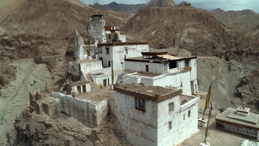 An aerial of white buildings built into a cliff on a rocky mountain