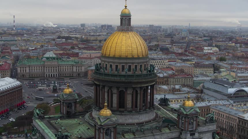 A tall domed building with beautiful architecture and statues overlooks a crowded city as traffic moves on the streets